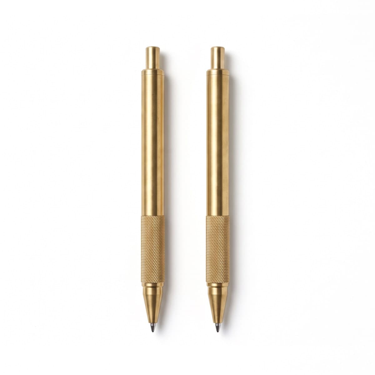 Two brass rollerball pens with knurled grips lying side by side